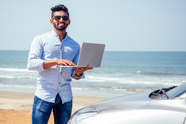 英俊、成功的印度男人，穿着时尚、体面的自由职业者，在海滩上用笔记本电脑工作。一个商人学生在印度洋岸边的夏日咖啡馆里图片下载