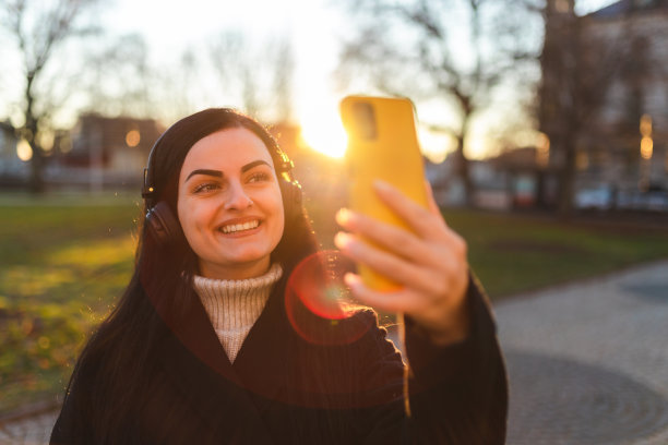 美丽的黑发女子戴着耳机在日落时分自拍图片下载