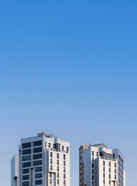 两个高大的住宅塔楼顶部的正面视图，带有蓝天和复制空间图片下载