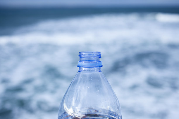 特写的透明打开塑料瓶没有盖子与选择性聚焦和散焦自然海洋背景。塑料回收概念。没有螺旋盖的塑料瓶。图片下载