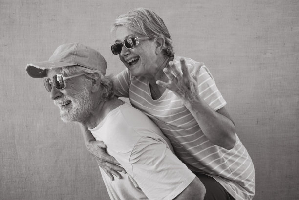 黑白照片，欢快的老夫妇玩得很开心，而男人背着他的妻子，老年退休人员戴着现代太阳镜图片下载