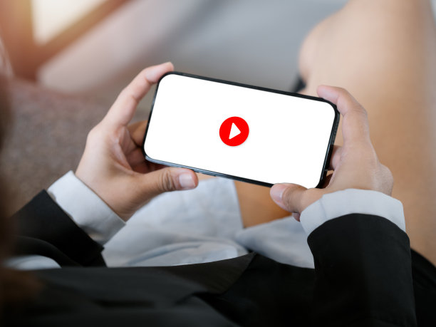 移动智能手机白色屏幕背景红色播放按钮图标，由商务女性双手横握。看电影，娱乐或社交网络内容，放松时间。图片下载