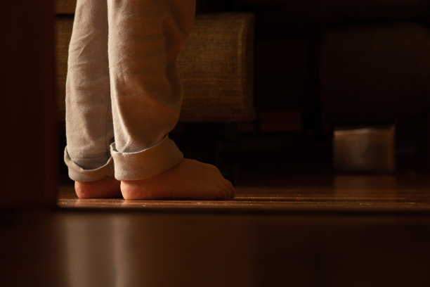 在一个黑暗的房间里，一个小男孩光着脚站在地板上图片下载
