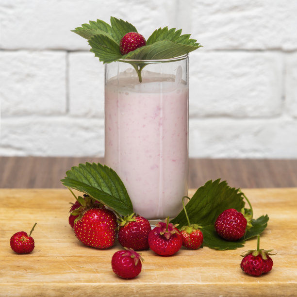 一杯以树叶为背景的草莓酸奶，草莓叶子和新鲜草莓图片下载