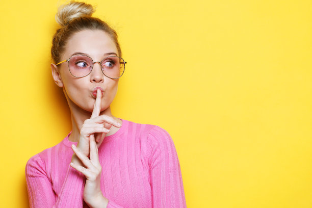 年轻的金发女子穿着作物粉红色毛衣和眼镜微笑在黄色背景图片下载