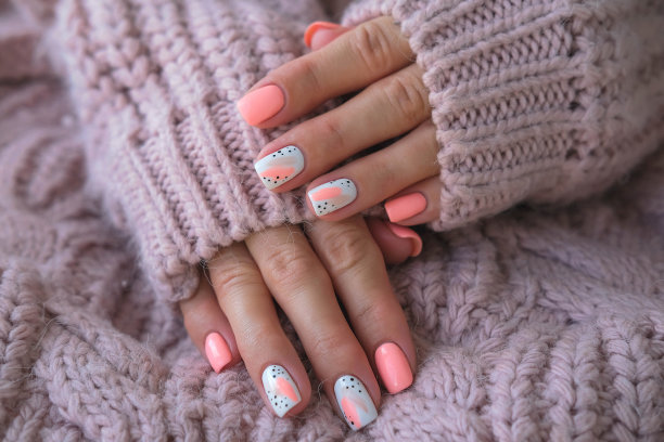 女人的手与一个美丽的美甲在温暖的粉红色针织毛衣。冬天的流行趋势，在粉色指甲上涂上指甲油和虫胶。图片下载