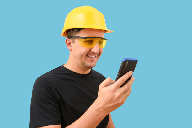 一个戴着头盔的工程师在蓝色背景上使用手机的肖像图片下载
