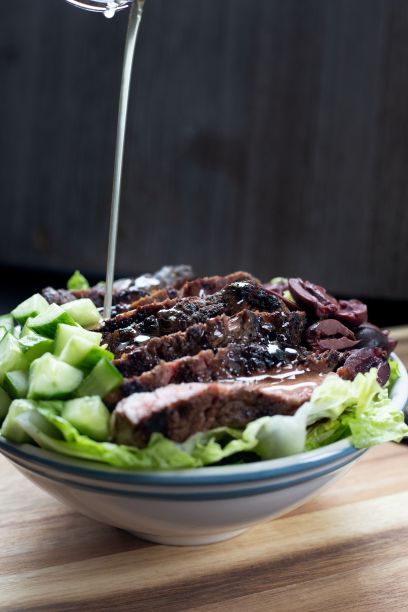 垂直特写的牛排沙拉在一个白色的盘子上，酱汁在木板上图片下载