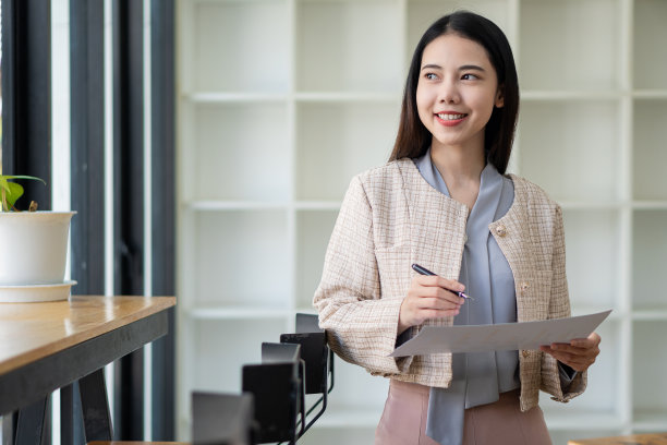 漂亮的微笑的亚洲女性自信地站在办公室看着窗外微笑，思考未来的成功。图片下载
