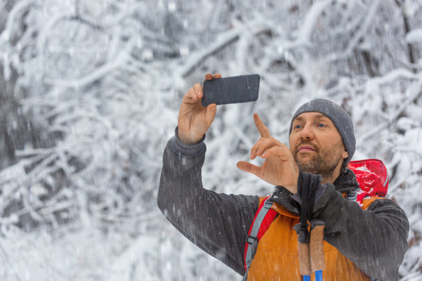 中年徒步旅行者在冬天的森林里用他的手机拍照。图片下载