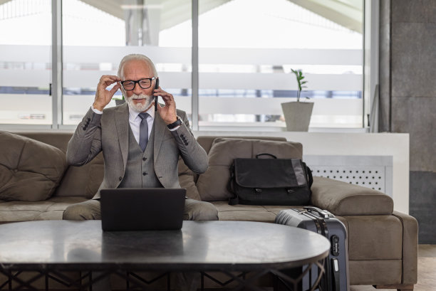 商人戴着眼镜边看笔记本电脑边讲智能手机。图片下载