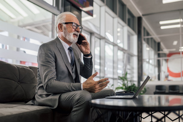 高级企业家在办公室边用笔记本电脑边用智能手机聊天。图片下载