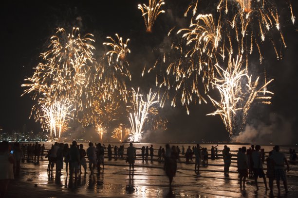 海滩上的新年庆祝活动。人们在水边看烟花。图片下载