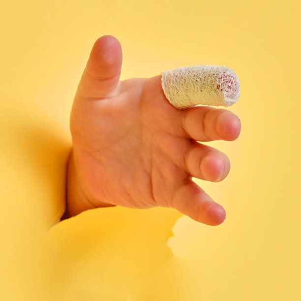 婴儿的手与包扎的手指在黄色工作室背景，特写。孩子受伤的食指用白色绷带包扎图片下载