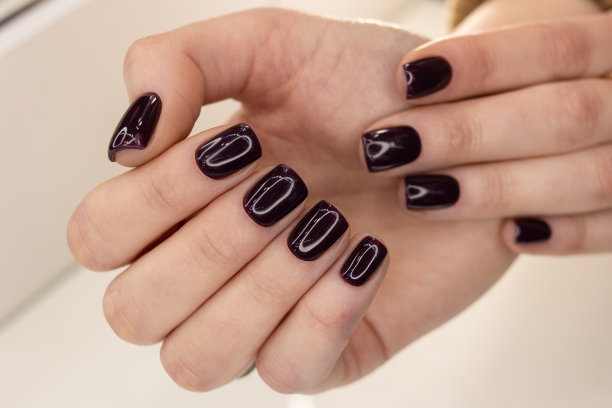 一个女孩的指甲上涂了深色指甲油。深色指甲，柔软的方形指甲。凝胶抛光涂料图片下载
