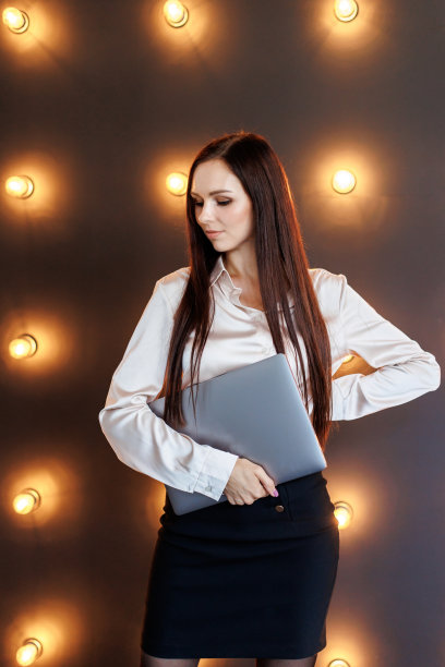 女人拿着笔记本电脑，站在工作室与照明灯在黑暗的背景。图片下载