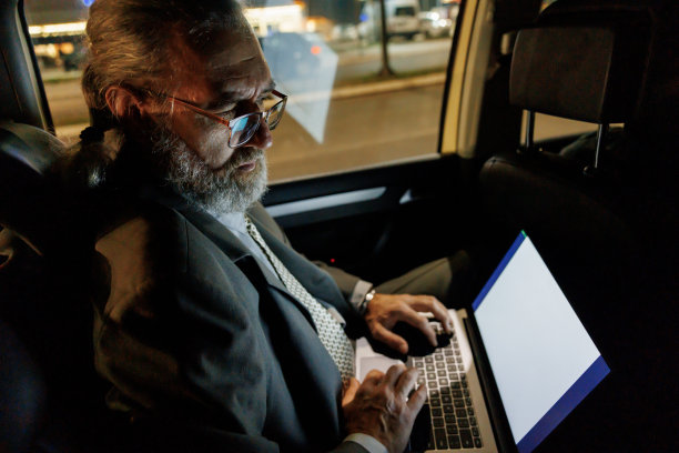 成熟的商人在晚上开车时坐在汽车后座上使用笔记本电脑图片下载