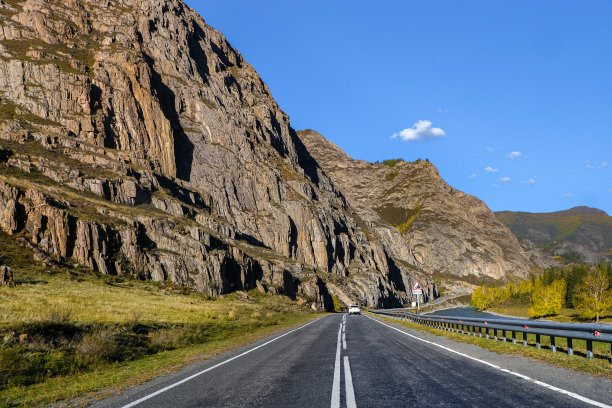 弯弯曲曲的柏油路穿行在高高的雪峰、黄色的沙漠、秋绿的森林和蓝天之间。高速公路上的汽车，背景是山上的风景图片下载