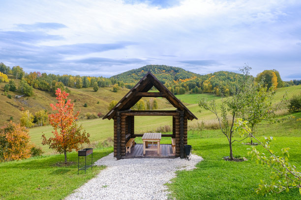 秋天山谷中供游客休息的地方。木制凉亭，房子的背景是绿色，黄色的草地和山峰在一个阳光灿烂的日子图片下载