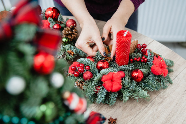 一位女装饰师在木制圆桌旁用云杉树枝、红色蜡烛、红色棉条和红色圣诞球做了一个圣诞装饰架。画框里只有手图片下载