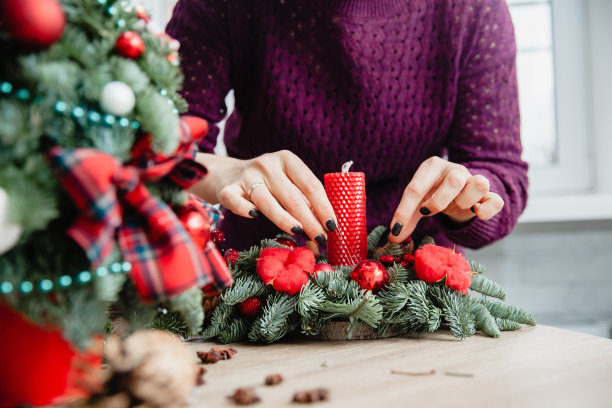 一位女装饰师在木制圆桌旁用云杉树枝、红色蜡烛、红色棉条和红色圣诞球做了一个圣诞装饰架。画框里只有手图片下载