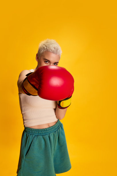 年轻的时尚女子短发摆出拳击手套的肖像，训练孤立在黄色背景。赢家图片下载