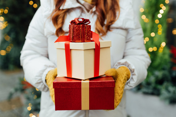 冬天的户外，妇女们手拿圣诞礼物。降雪。冷杉树，后面有花环。购物的概念，节日和快乐的圣诞节。图片下载