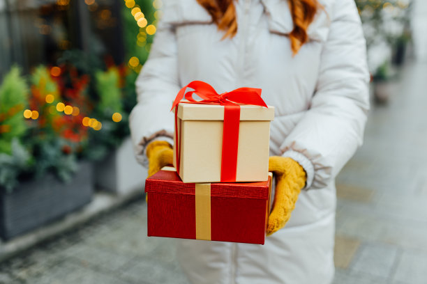 冬天的户外，妇女们手拿圣诞礼物。降雪。冷杉树，后面有花环。购物的概念，节日和快乐的圣诞节。图片下载