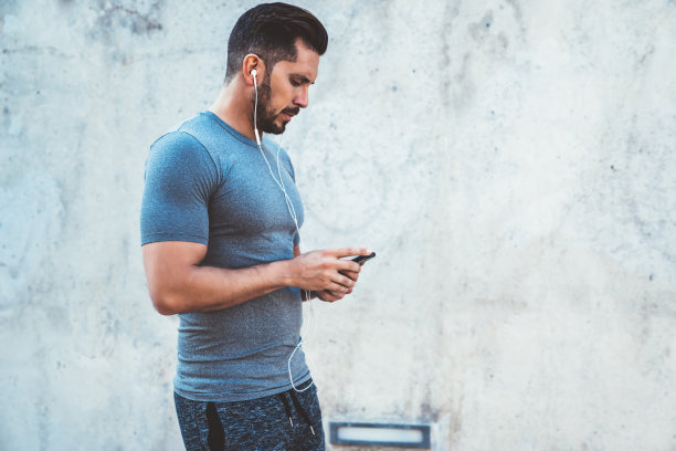 严肃的千禧男博主戴着耳机查看智能手机上的健身音乐下载通知，年轻的20多岁运动员使用应用程序记录活动结果和燃烧脂肪图片下载