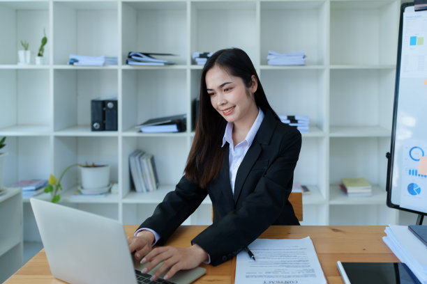 一名年轻的亚洲女性在凌晨使用电脑和办公桌上的财务文件时露出笑容的肖像图片下载