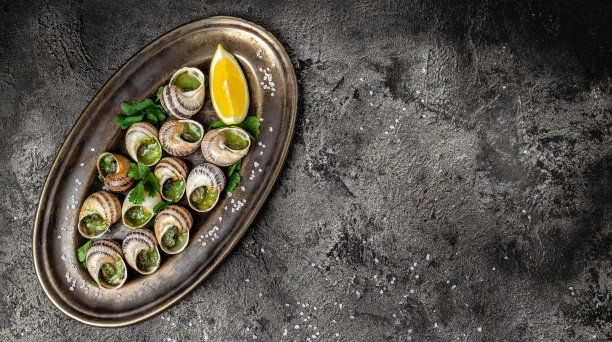 黑底烤蜗牛配黄油和香料。烤蜗牛配酱，勃艮第蜗牛。美味的食物。法式美食概念，长条旗格式。俯视图图片下载