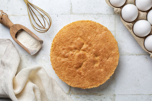 刚刚烤好的普通香草海绵蛋糕放在铁架上，白色的桌子正上方。蓬松、滋润、浓郁的雪纺蛋糕，两层，自制。烹饪器具和食材背景。图片下载