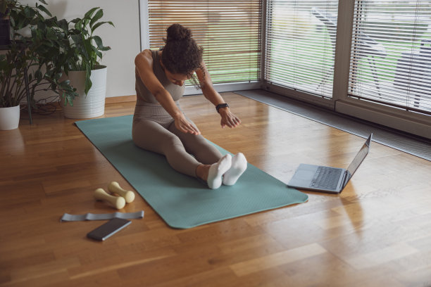 一名女子在家用笔记本电脑做伸展运动。室内锻炼，瑜伽，普拉提项目图片下载
