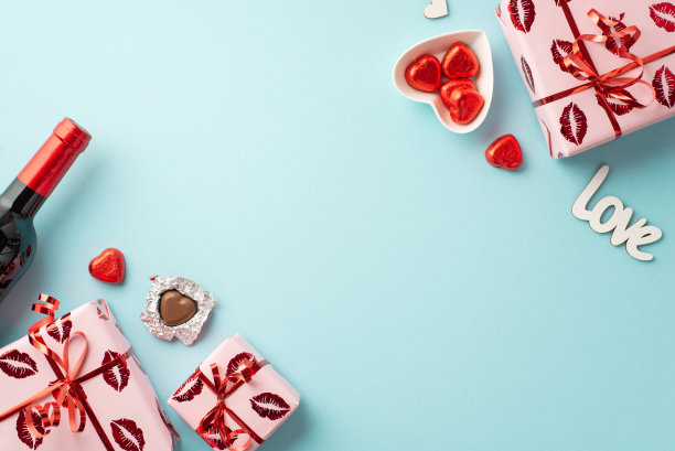 情人节的概念。顶部视图照片礼盒包装与亲吻嘴唇图案酒瓶和心形盘子与巧克力糖果在孤立的浅蓝色背景与复制空间图片下载
