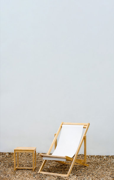 沙滩椅在卵石与白色混凝土墙背景，吊床椅与木桌在白色油漆水泥背景，垂直横幅与复制空间文本春夏假期概念图片下载