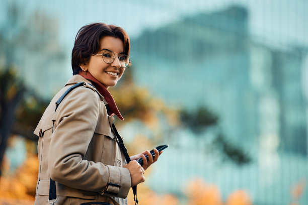 年轻快乐的女商人在城市中使用手机，看着相机。图片下载
