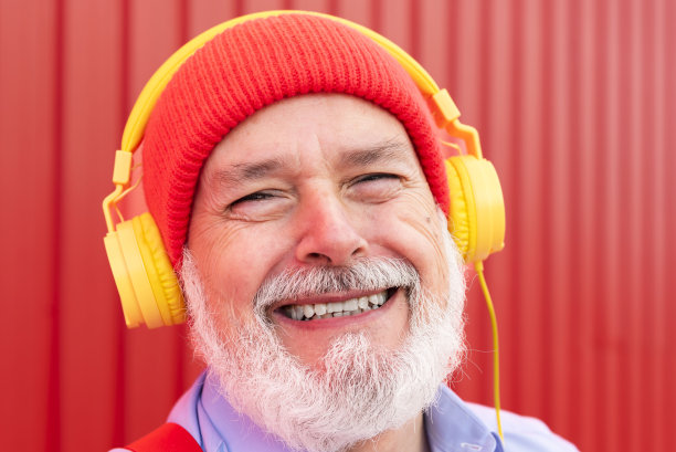 一个带着耳机听音乐的快乐的潮人退休人员的特写肖像图片下载