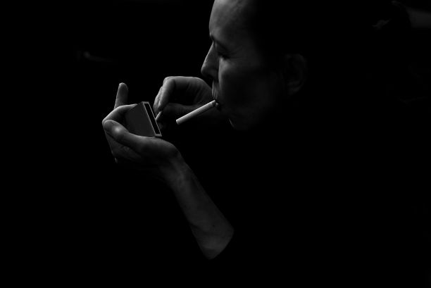 灰色的一个女人拿着点燃的香烟在她的手在一个黑暗的背景图片下载