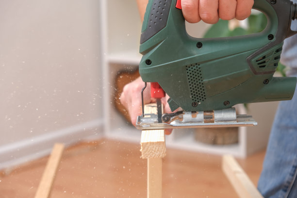 一个木匠大师的手手里拿着一个电动拼图锯正在切一块木头。男性用锯齿锯切割木材。一个木匠在家庭作坊里用拼图锯木头。图片下载