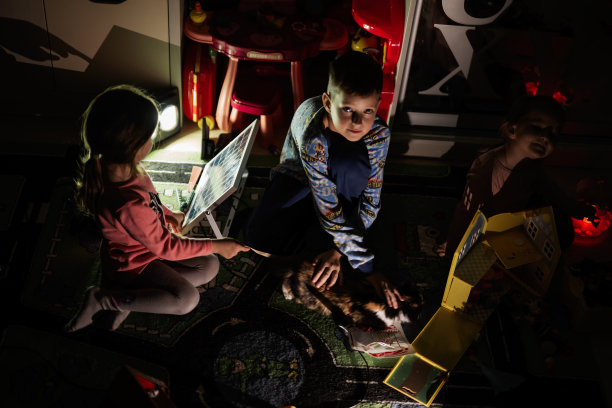 停电期间，孩子们在家里用替代照明和小猫玩耍。图片下载