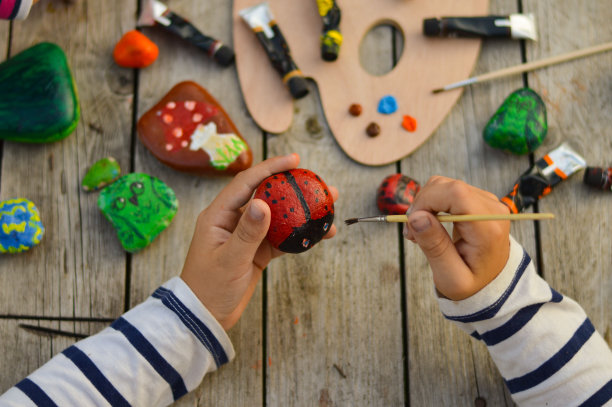 一个孩子用丙烯酸颜料在石头上画瓢虫的详细图片。家庭爱好是真实的。石头上的艺术品。图片下载
