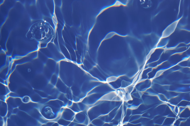 离焦模糊透明蓝色颜色清晰平静的水面纹理与飞溅和气泡。潮流抽象的自然背景。水波在阳光下带有焦散。碧水浪花闪闪发光图片下载