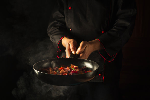 在厨房里煮新鲜蔬菜。厨师正拿着热气腾腾的煎锅。有广告空间的亚洲美食酒店创意。图片下载