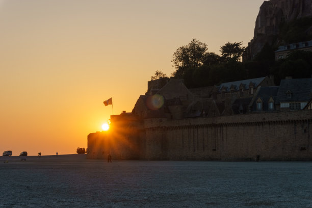 法国诺曼底，夏夜低潮时，太阳在日落时的圣米歇尔山入口图片下载