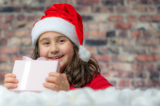 孩子穿着圣诞老人的红布打开一个小礼品盒。图片下载
