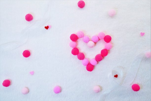 心形符号由情人节灵感绒球制成，白色背景上有粉色圆点图片下载