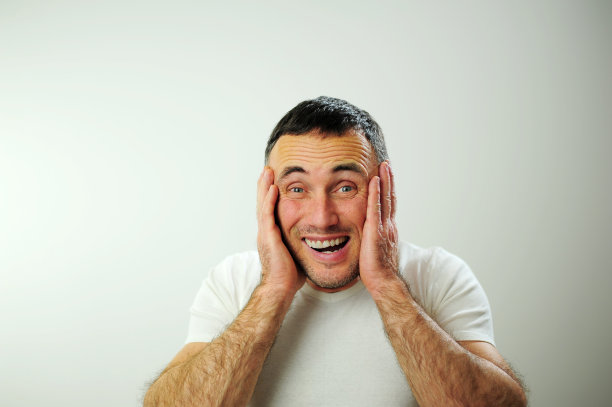 赢得有趣的假期旅行不同的快乐积极情绪的一个成年男子与灰色黑色的头发打开有趣的快乐的蓝眼睛白色t恤灰色背景皱纹额头伸出舌头图片下载