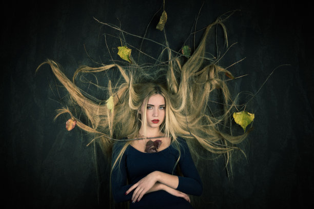 一个白人女性在工作室里摆姿势，秋天的树叶在她金色的毛茸茸的头发上，为万圣节做准备图片下载