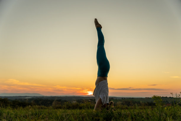 日出时，一名女子在风景上练习倒立图片下载
