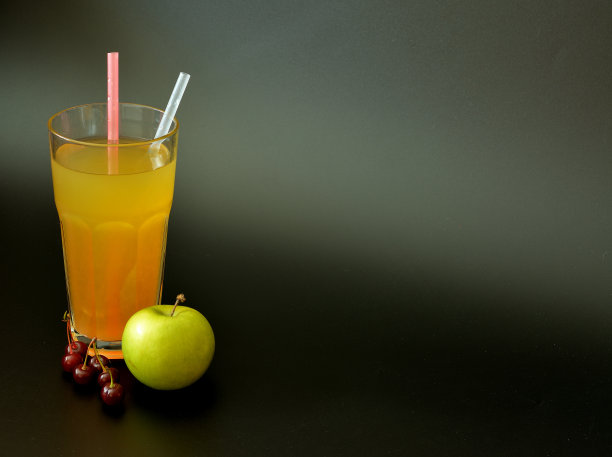 一大杯果汁，黑色背景上有吸管，旁边是一个绿苹果和一把成熟的樱桃。图片下载
